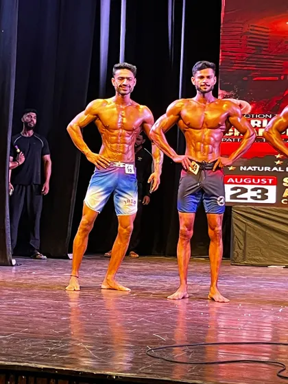 My men's physique athletes standing side-by-side on stage, both in incredible shape. This is the standard we aim for.