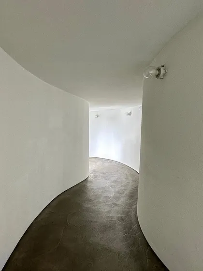 A curved interior corridor within the Gehry building. The simplicity of the white walls and exposed bulb emphasizes the pure, sculptural quality of the space.