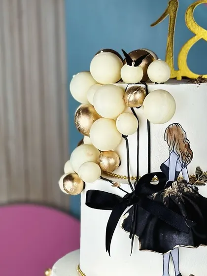 Understated luxury. This minimalist white, black, and golden cake for an 18th birthday is a masterpiece of simplicity and elegance, featuring a chic silhouette and balloon accents.