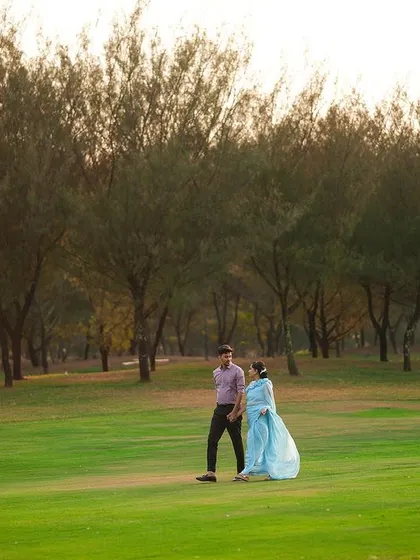 A wide, cinematic shot of a couple walking in a large, open field, showcasing the scale and beauty of the landscape.