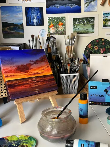 The vibrant sunset painting resting on a mini easel on my desk, with my brushes and water jar nearby.