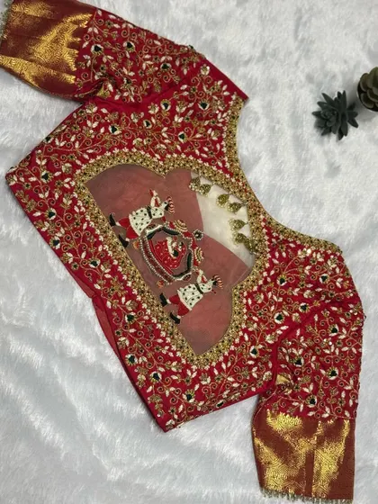 A classic bridal look that never fails. This fiery red blouse features a detailed palanquin (doli) scene embroidered within a heart-shaped back cutout, framed by intricate floral zardosi work. This is storytelling through thread.