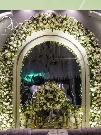 A photo booth area for an enchanted forest-themed event, featuring a large arch of white roses and a plush grey sofa.