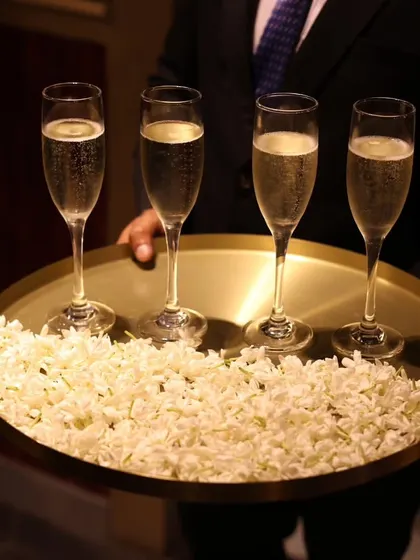 A server holds a tray of champagne flutes, elegantly presented on a bed of fresh jasmine flowers. It's this attention to detail that defines the Rosé luxury experience.
