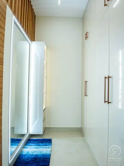 A view of the walk-in closet area, featuring glossy white handle-less wardrobes and a full-length mirror with integrated lighting. A wooden slat wall adds a touch of warmth and texture.