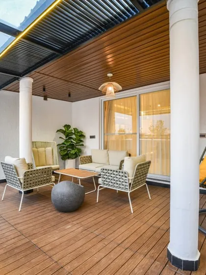 Another view of the spacious balcony, highlighting the cozy swing chair and comfortable seating arrangement under a pergola with a glass roof, perfect for enjoying any time of day.