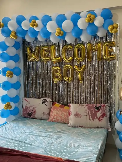 A bedroom setup to welcome a new baby boy, with a blue, white, and gold balloon arch and "Welcome Boy" foil letters.