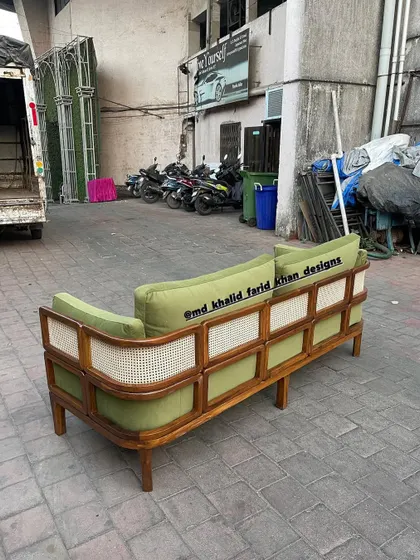 A similar sofa design, this time upholstered in a vibrant olive green fabric that contrasts beautifully with the warm teak and natural cane.