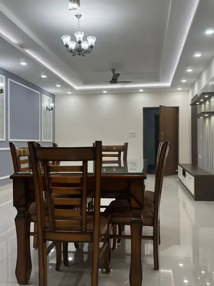 A view of the dining and living area in a newly completed project. The image highlights the spaciousness, the false ceiling with cove lighting, and the placement of the TV unit.