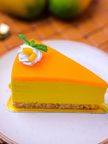A slice of our seasonal Mango Cheesecake, featuring a creamy mango-infused filling and a vibrant mango jelly topping on a vanilla crumb base.