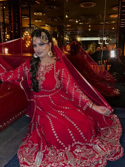 Another angle of the stunning red Pakistani bridal look, showing how the outfit flows beautifully. The makeup is designed to be captivating from every perspective, ensuring the bride looks perfect in all her photos.