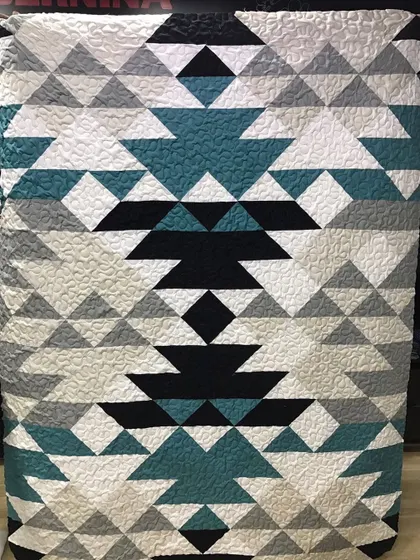 A modern quilt with a bold, tribal-inspired geometric pattern in shades of teal, black, and grey.