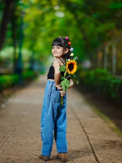 A playful and shy pose, with the little girl hiding a sunflower behind her back.
