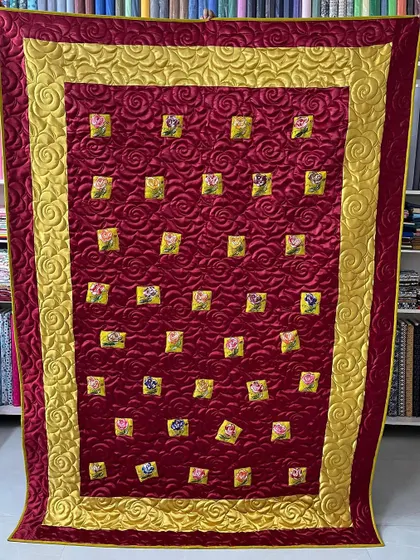 A luxurious quilt with a rich red background, gold border, and small, floating floral blocks.