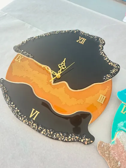 A modern, abstract resin clock with a striking black and orange color-blocked design, edged with black crystals.