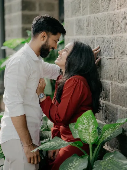 An intimate moment between a couple, leaning against a stone wall surrounded by greenery. Their joyful expressions show the fun and connection we capture during our sessions.