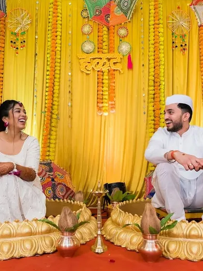 A happy, relaxed moment between the bride and groom at their haldi, seated against a colourful and festive backdrop.