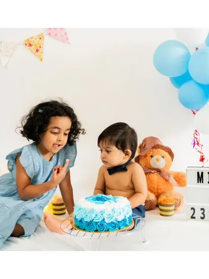 A big sister helps her baby brother with his first birthday cake. Sibling involvement makes milestone sessions even more special and memorable.