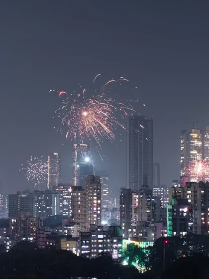 A wide shot of the Mumbai skyline during Diwali, with multiple fireworks lighting up the night over the city's countless buildings.