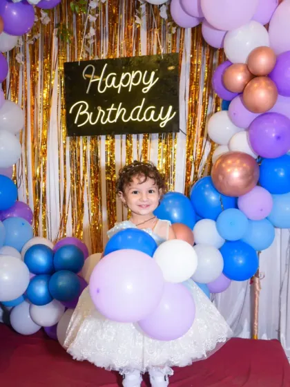 A happy birthday girl surrounded by a sea of colorful balloons. Her bright smile shows the pure joy of her special day.