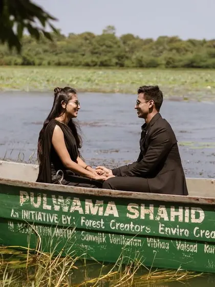 A beautifully framed shot of the couple in the boat, with lush green foliage in the foreground. This composition adds depth and a sense of privacy to their romantic moment.