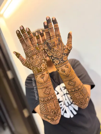 A full and heavy bridal design with traditional motifs. The client is happily showing off the complete work, covering her hands and forearms.