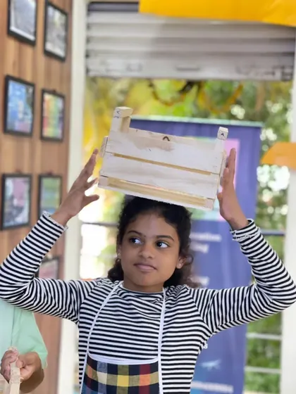 This young builder playfully balances the wooden crate she just finished assembling. Our woodworking projects often create useful items to take home.