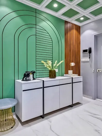 An artistic and modern foyer design featuring a mint green accent wall with geometric line art. The simple white console table and gold stool add a touch of elegance and color.