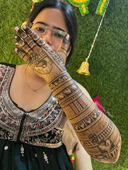 A full-arm bridal design with peacocks and elephants, showcased by a happy bride.