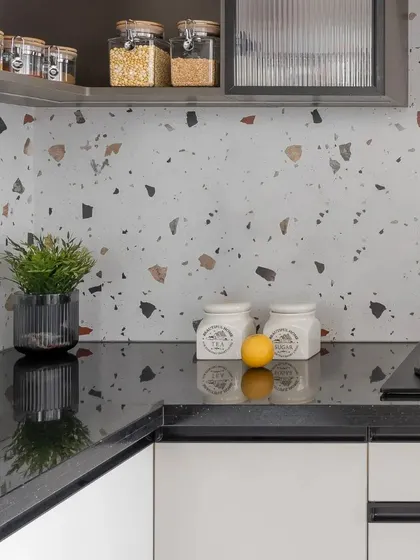 A detail shot of a kitchen with white cabinets, a black countertop, and a terrazzo-inspired backsplash. The open shelving provides easy access to spices and everyday items.