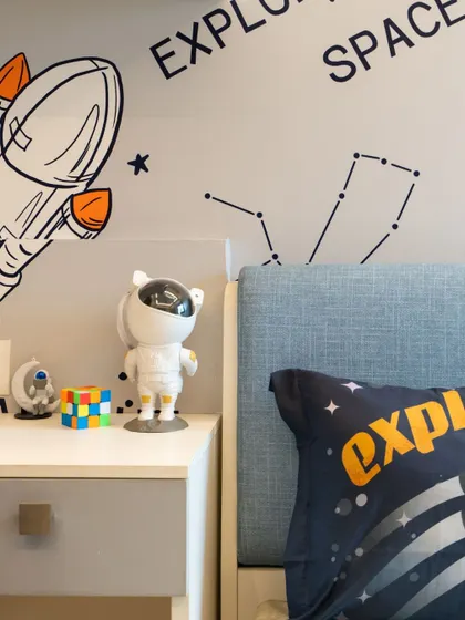 A detail shot of the bedside table in the space-themed room, featuring a cute astronaut-shaped lamp and other themed decor items.