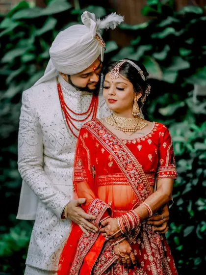 A classic portrait of the couple in their stunning red and white wedding attire. The groom's loving gaze and the bride's serene expression create a timeless image of marital bliss.