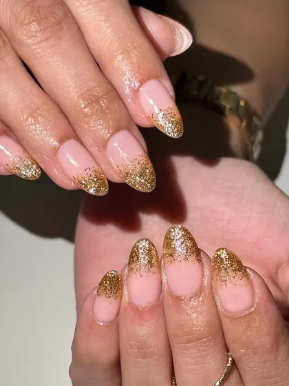 A classic choice for any celebration, these almond-shaped nails feature a soft nude base with a cascading gold glitter gradient from the tips. This French ombré style offers a glamorous yet sophisticated look.