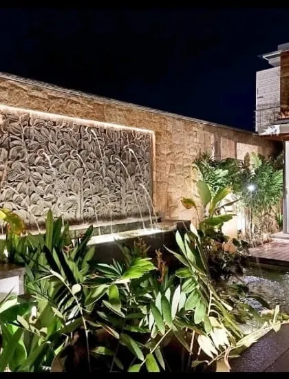 A custom-designed water feature illuminated at night, creating a serene and high-end ambiance. This stone-carved waterfall, integrated with lush tropical foliage and subtle lighting, exemplifies my work in creating unique focal points for luxury properties.