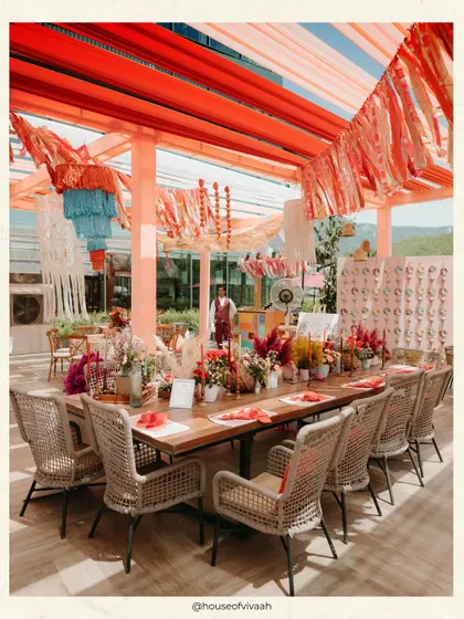 A long wooden community table at the Pahadi Mehendi, set under a canopy of rust-colored tassels and drapes, creating a warm and inviting space for guests to gather.