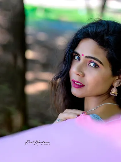 A close-up shot focusing on the details of the pink saree and the model's expression. The soft, natural light of the park setting enhances the gentle and elegant mood.