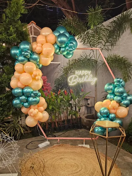 A modern hexagonal arch with a teal and peach balloon arrangement, perfect for an outdoor garden or terrace party.
