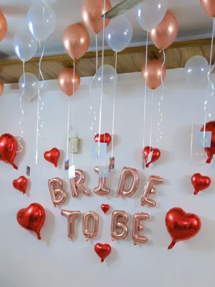 A lovely 'Bride to be' setup with rose gold and white balloons on the ceiling, from which personal photos are hung with ribbons.