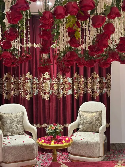 A cozy seating area within the decorated room. The chairs are placed against a backdrop of red curtains and a ceiling of hanging red roses.