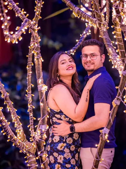 A close-up portrait with the couple framed by trees wrapped in fairy lights. The purple backlighting adds a unique and colorful touch to this romantic night shot.