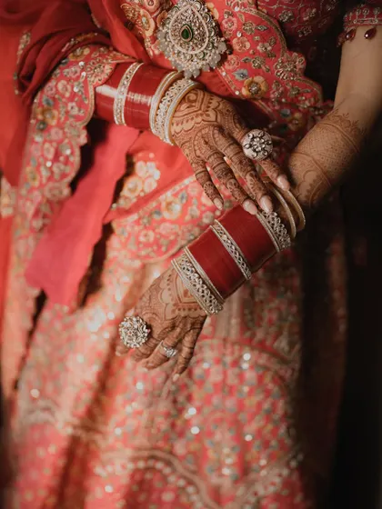 A close-up of the bride's hands, showcasing her beautiful red chooda bangles and intricate mehndi.