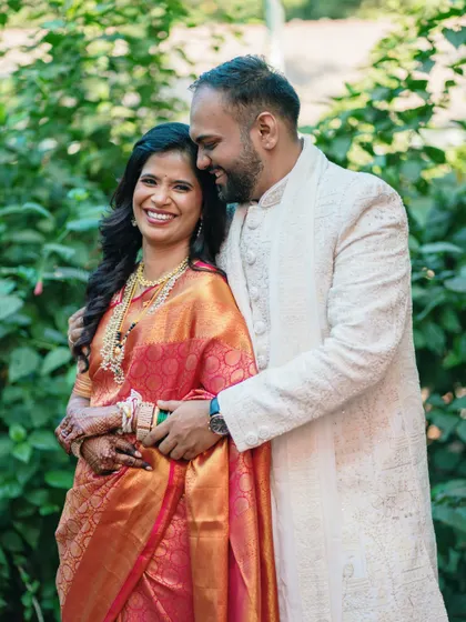 A warm embrace amidst lush greenery, this photo captures the couple's comfortable and affectionate bond in their beautiful traditional outfits.