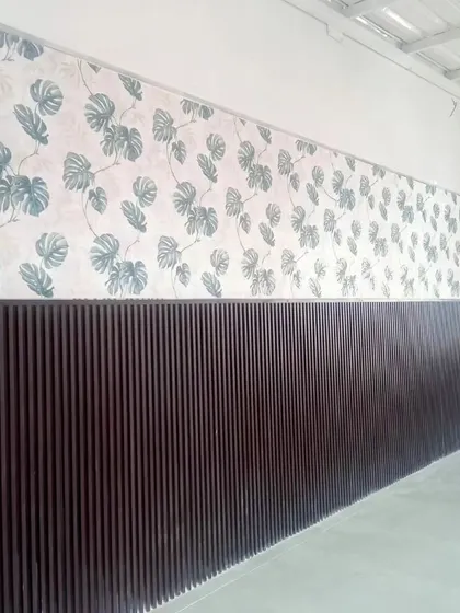 A wall featuring a monstera leaf wallpaper above dark wood paneling, creating a stylish and modern contrast.