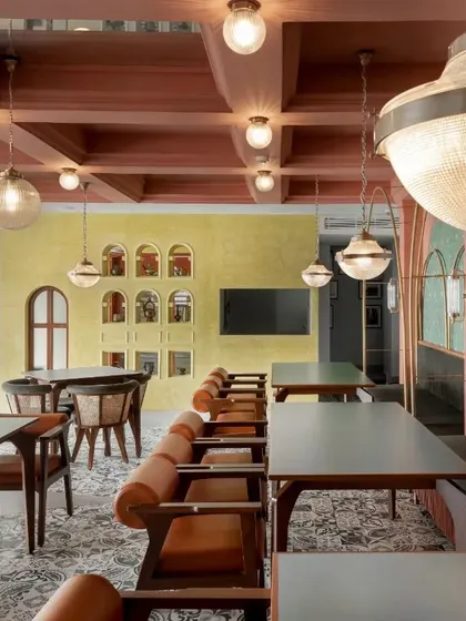 A view across the restaurant showing the interplay of different zones. A wall of arched niches in a contrasting yellow-green stucco finish serves as a vibrant backdrop.