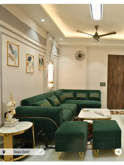 An emerald green L-shaped sofa brings a sense of luxury to this living room at Saya Gold. The gold and marble side table and classic wall molding complete the elegant look.