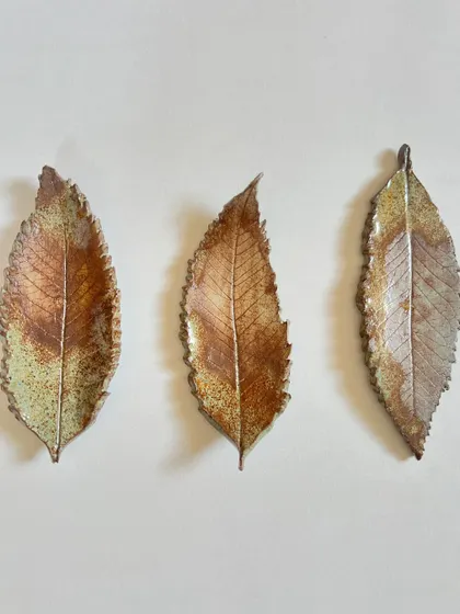 A set of three delicate, elongated ceramic leaves, each with unique textures and rustic glaze effects.