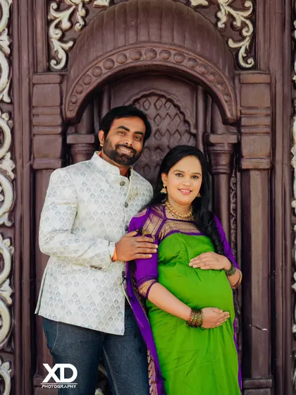 A happy couple portrait against a carved wooden door, showcasing a beautiful green and purple saree.