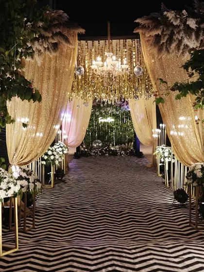 A stunning Sangeet entrance combining gold sequin drapes, a chevron-patterned aisle, and a personalized welcome sign.