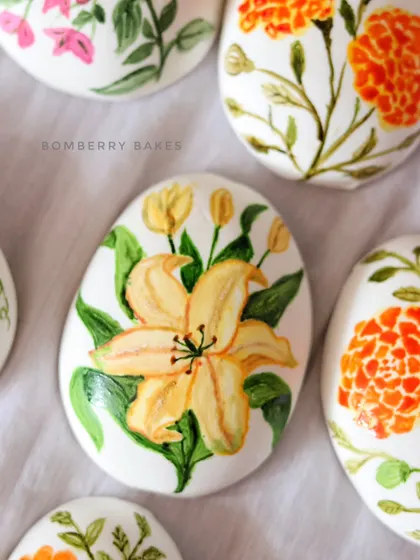 A close-up of a hand-painted Easter egg made from homemade cashew marzipan, featuring a beautiful yellow lily.