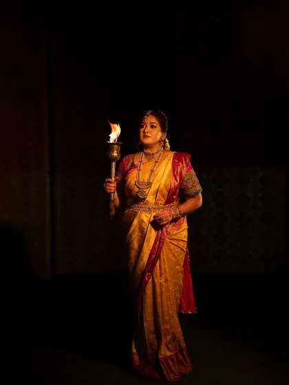 A full-length shot of Meghana Raj against a dark background, with the torch as the only source of light. A truly powerful and artistic image.